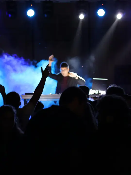 DJ en un escenario con luces y humo ante el público en una fiesta mayor