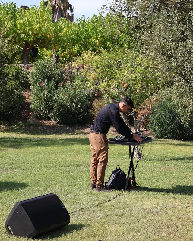 DJ montando el equipo de sonido en un evento al aire libre entre árboles